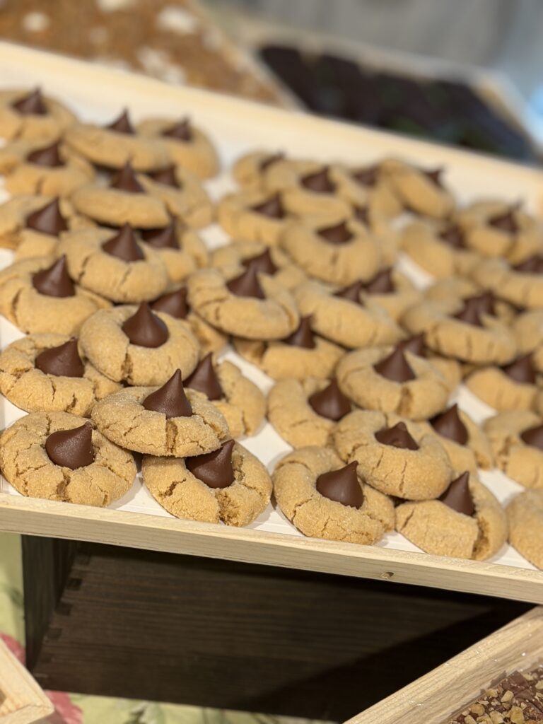 Pile of round peanut butter cookies with a chocolate center on a wooden tray, arranged for display in a bakery.