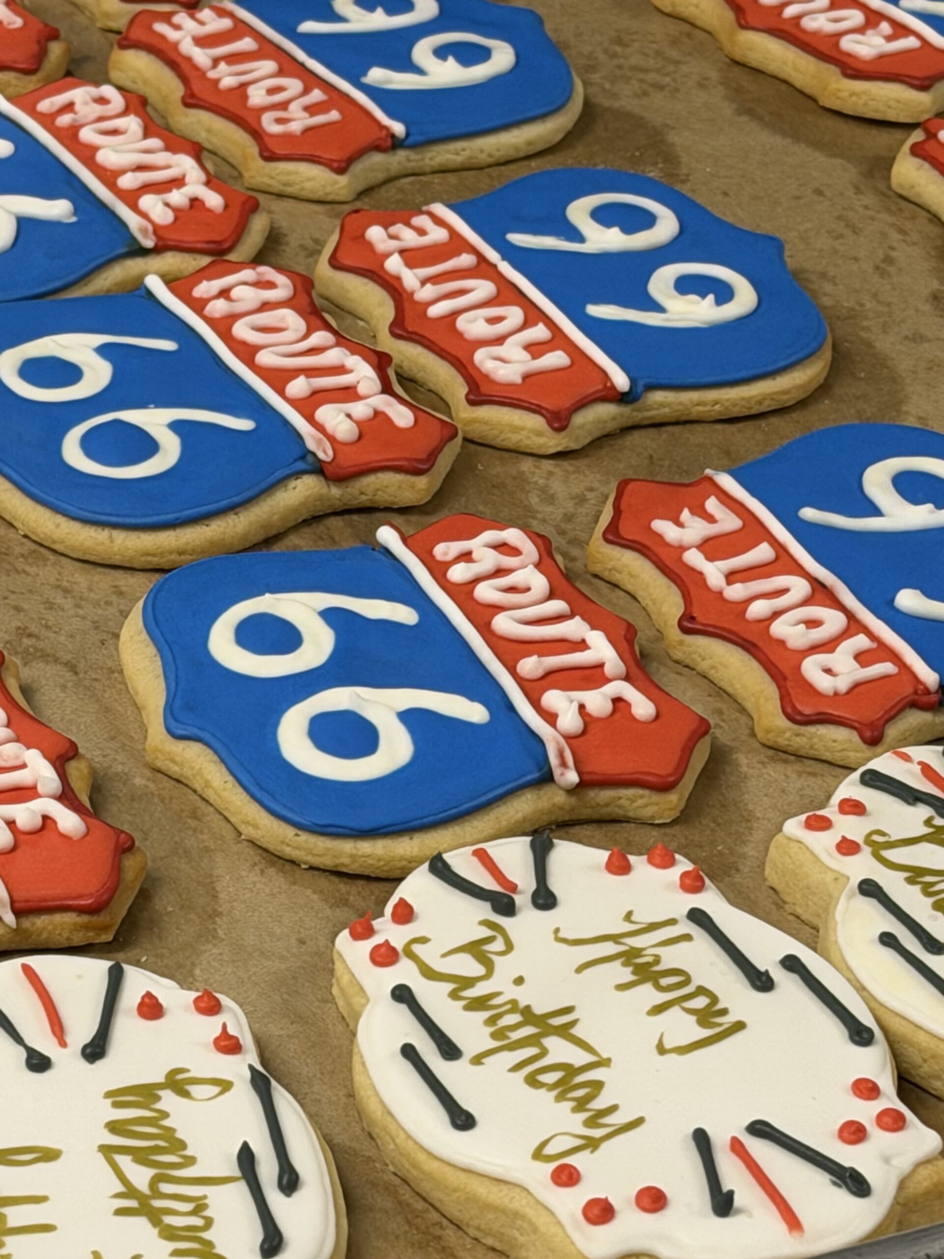 Decorated sugar cookies on a tray, blue circular pieces with a white '60' and red banner accents for a 60th birthday celebration, with white icing details.