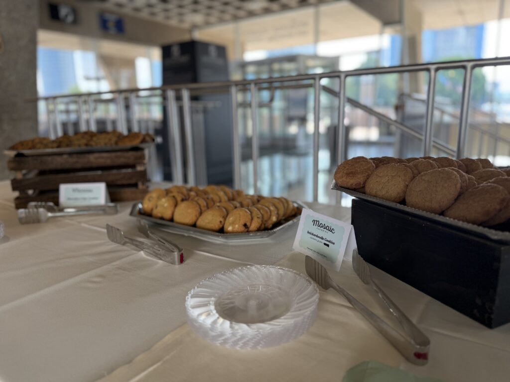 Buffet table with trays of cookies and pastries on a white tablecloth at a bright venue, blurred background.