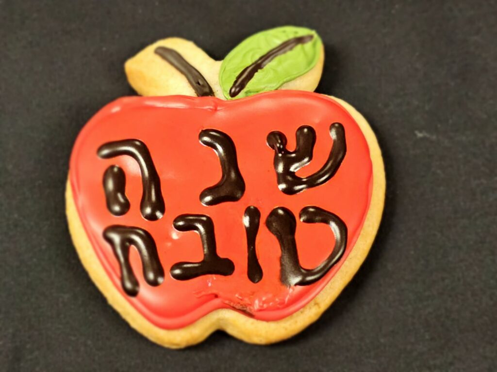 Heart-shaped cookie decorated to look like a red apple with a green leaf and a black I LOVE YOU message across the surface.