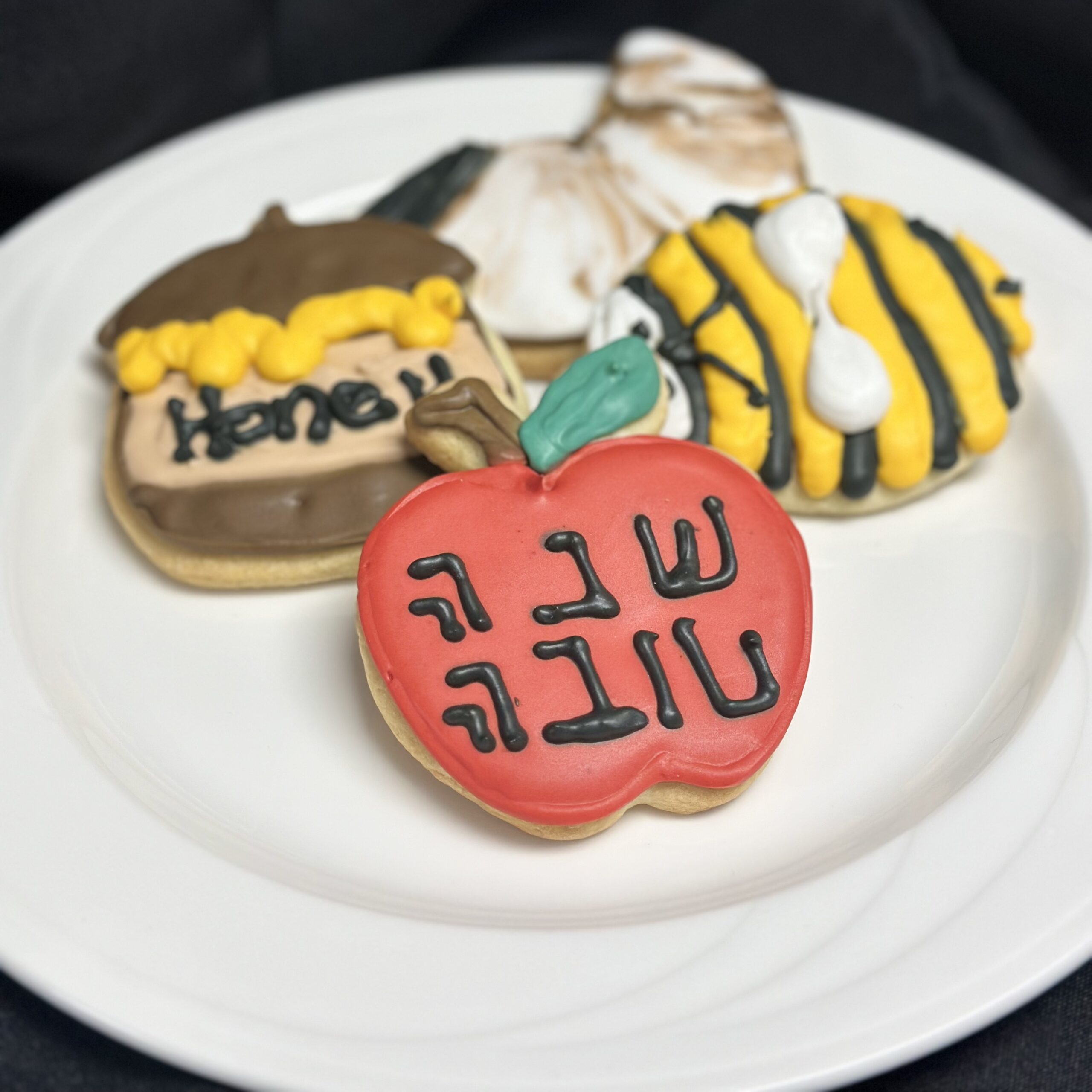 Decorated cookies on a white plate, including a red heart-shaped cookie in front and colorful striped cookies in the background.